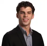 A male business consultant wearing a blue blazer, checkered shirt, and smiling, with short brown hair.